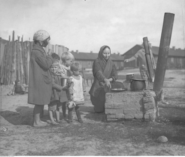 Bieda i głód. Taka była codzienność większości mieszkańców przedwojennej wsi. Na zdjęciu grupa dzieci z Żoliborza przy prowizorycznej kuchni, na której kobieta przyrządza posiłek.