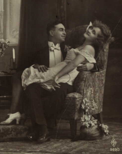 Mężczyzna w fotelu i kobieta siedząca na jego kolanach. Pocztówka z początku XX wieku